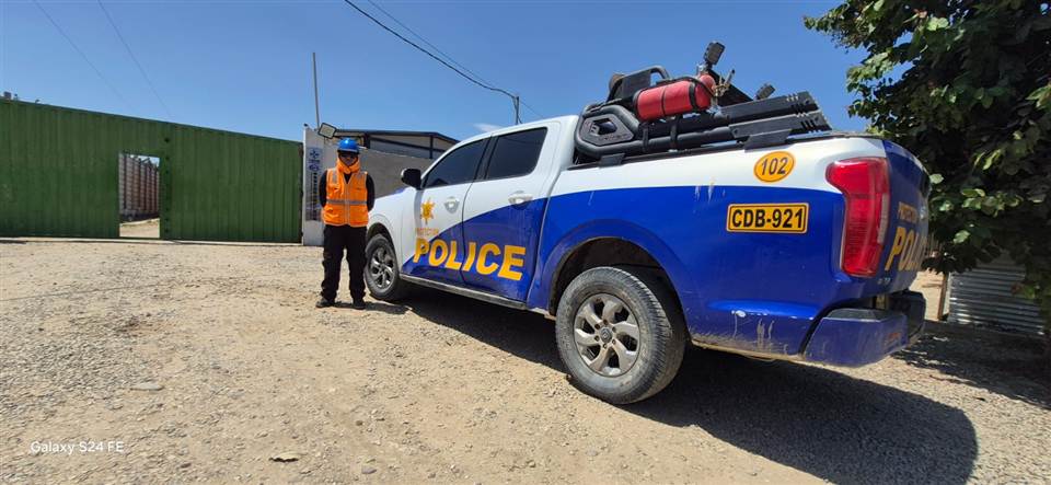 Agente de Protection Police con casco y chaleco junto a una camioneta de la empresa en la entrada de una obra.